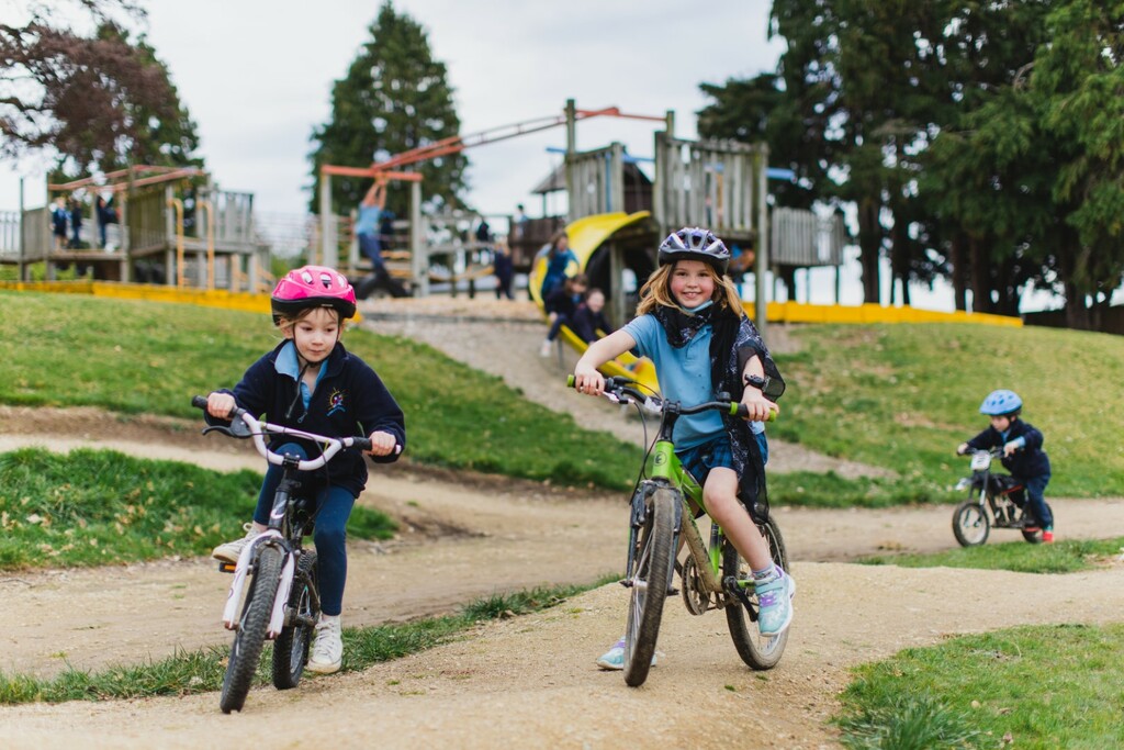 Children in uniform on bikes in the outdoor area at school.